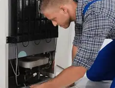 Refrigerator repair technician servicing the compressor and condenser area in Mobile, AL
